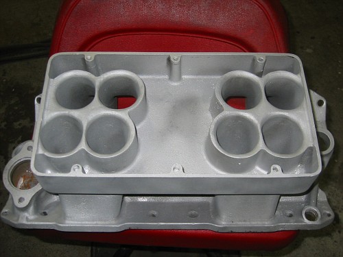 Aluminum intake manifold with eight ports, resting on a red surface