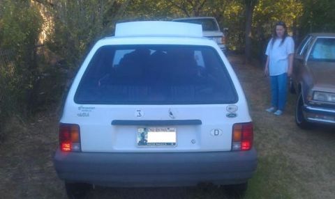 1991 Ford Festiva - Rear view of a white 1991 Ford Festiva parked outdoors with a person and another vehicle nearby.