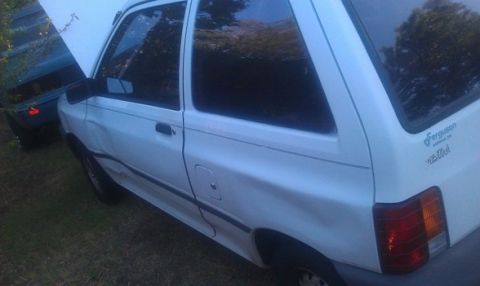 1991 Ford Festiva - A white hatchback is parked next to another vehicle, with its hood open.