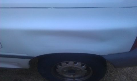 1991 Ford Festiva - A dent is visible on the rear quarter panel of a white car, near the wheel.