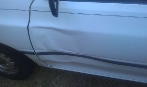 1991 Ford Festiva - Side view of a white 1991 Ford Festiva showing a large dent on the door panel.