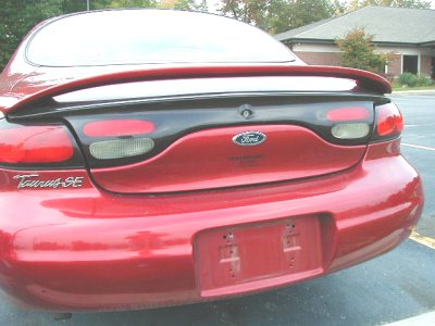 1997 Ford Taurus - Close-up rear three-quarter view of a red Ford Taurus SE sedan showing the body-color pedestal spoiler on the decklid, the smoked full-widt…