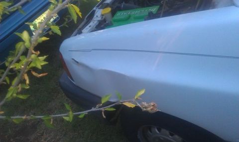 1991 Ford Festiva - Close-up of a damaged white car fender, showing a dent and a pinstripe.