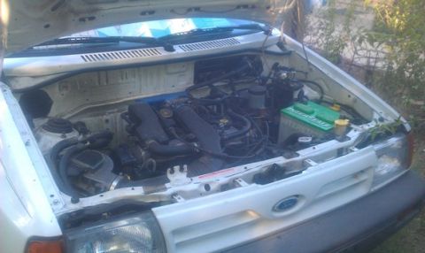 1991 Ford Festiva - The engine compartment of a white vehicle is visible with the hood raised, revealing the engine and battery.