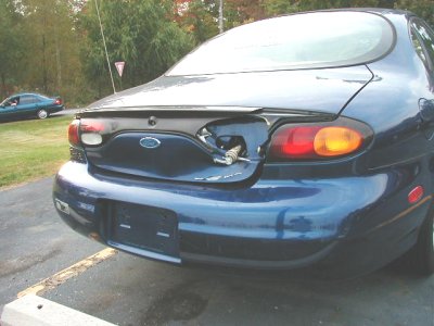 1997 Ford Taurus - The rear of a blue sedan is shown with its fuel door open, revealing the gas cap and hose.