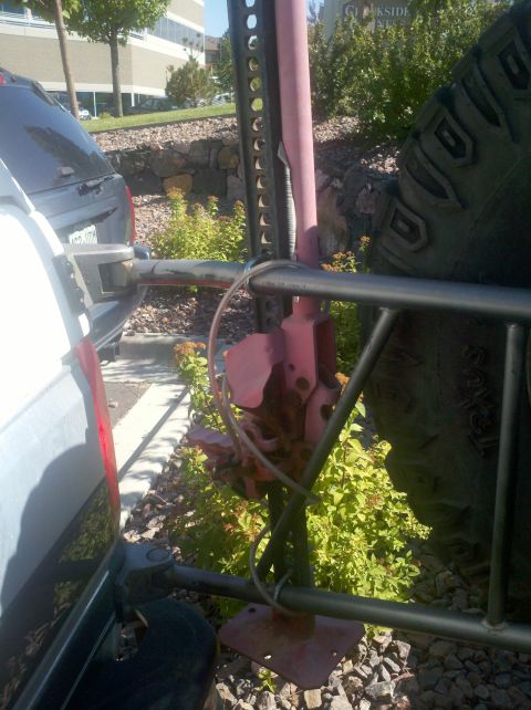 1996 Ford Bronco - A high lift jack is mounted to the rear bumper of a vehicle, next to a spare tire.