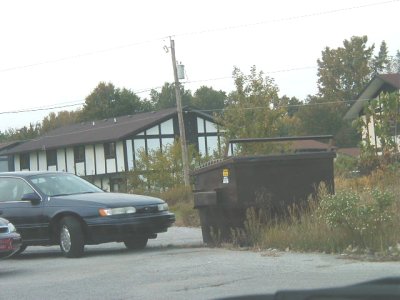 1997 Ford Taurus - A dark sedan is parked near a large dumpster in front of some buildings.