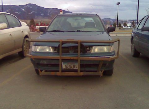 2006 Ford E350 - A dark sedan is parked in a lot, fitted with a substantial, custom-made metal bull bar across its front end.