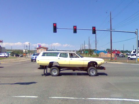 2006 Ford E350 - A heavily modified station wagon with an elevated chassis and oversized wheels drives through an intersection.