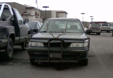2006 Ford E350 - A car with a bull bar and deer antlers is parked in a lot next to a pickup truck.