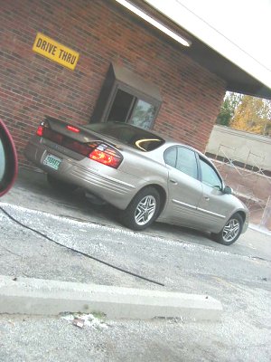 1997 Ford Taurus - A silver sedan is parked near a brick building with a 'Drive Thru' sign.