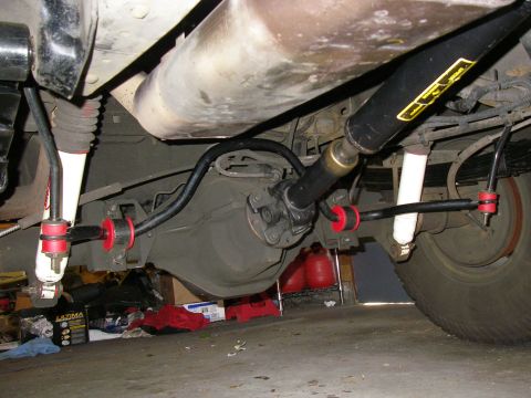 1990 Ford Bronco - View under the rear of a truck showing a rear anti-sway bar with red polyurethane bushings and end links mounted to the axle, white-bodied…