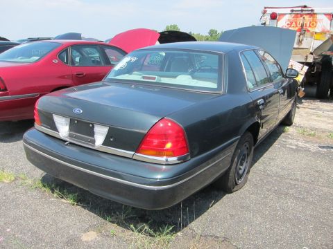 1991 Ford LTD Crown Victoria - This Ford Crown Victoria has a flat tire and is parked in a junkyard next to other vehicles.