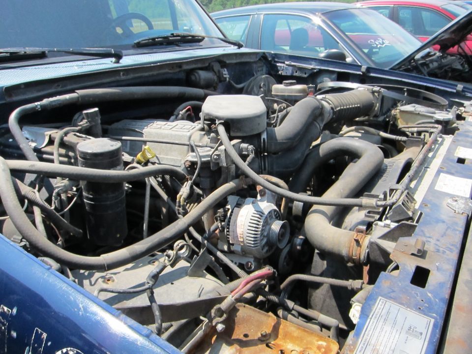Engine bay of a blue vehicle, with other cars visible in the background
