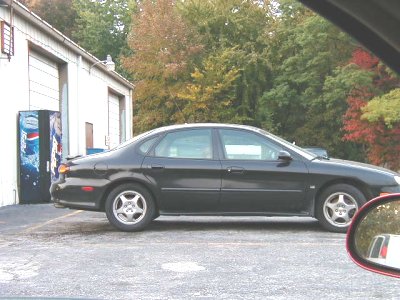 1997 Ford Taurus - A black sedan is parked outside a building with trees in the background.