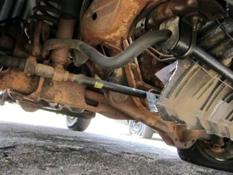 1991 Ford LTD Crown Victoria - The underside of a vehicle reveals heavily rusted suspension parts and a drive shaft.
