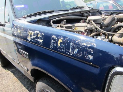 1991 Ford LTD Crown Victoria - A blue police truck with the hood open, revealing the engine and worn 'STATE POLICE' lettering on the fender.