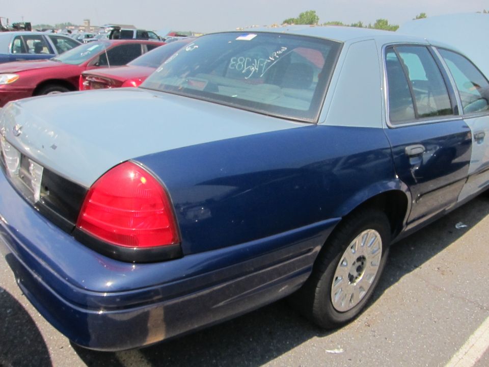 Rear quarter view of a two-tone blue and gray Ford Crown Victoria. The car has a two-tone paint job and is parked in a lot with other vehicles