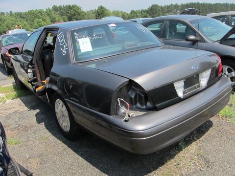 1991 Ford LTD Crown Victoria - Rear view of a damaged Ford Crown Victoria in a junkyard, showing missing taillight and body damage.