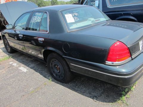1991 Ford LTD Crown Victoria - A dark sedan with a flat tire sits in a lot next to another vehicle.
