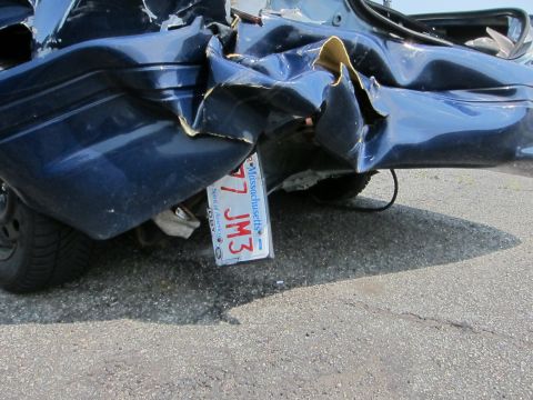 1991 Ford LTD Crown Victoria - The rear of a severely damaged blue sedan, showing a bent bumper and a Massachusetts license plate.
