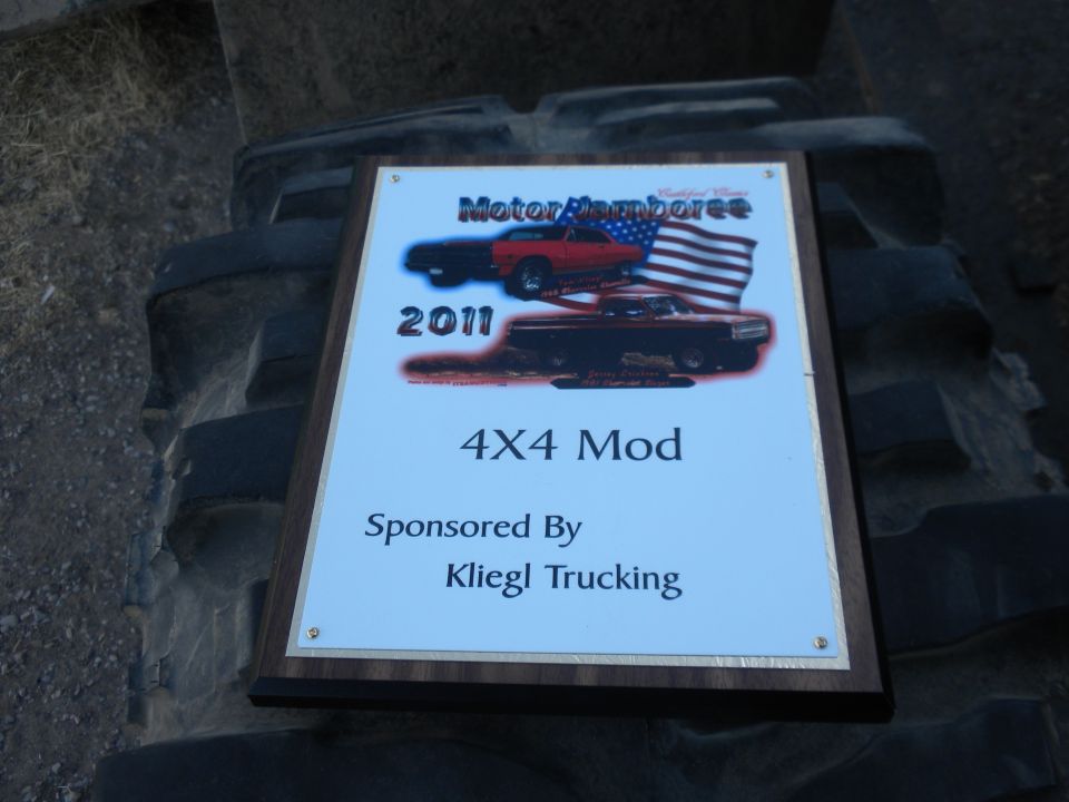 Plaque reading 'Motor Jamboree 2011 4X4 Mod Sponsored By Kliegl Trucking' resting on a large tire