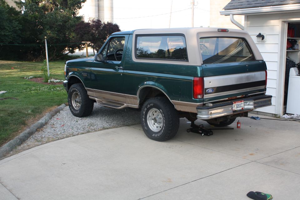 Green Ford Bronco parked in driveway, jack under rear axle