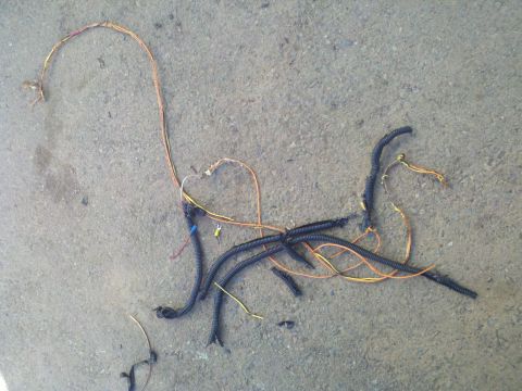 1986 Ford Bronco - A tangled automotive wiring harness lies on a concrete surface, showing black tubing and exposed wires.