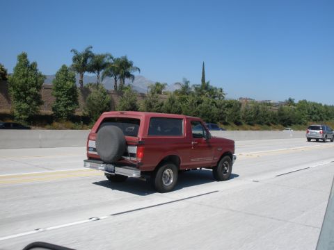 1989 Ford Bronco - A red Ford Bronco is seen from behind on a sunny day, traveling on a freeway.