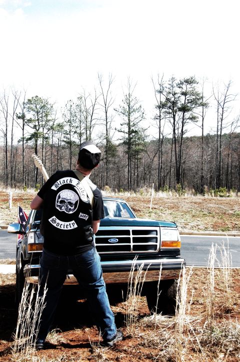 1993 Ford Bronco - A man holding a guitar stands in front of a dark green 1992 Ford truck.