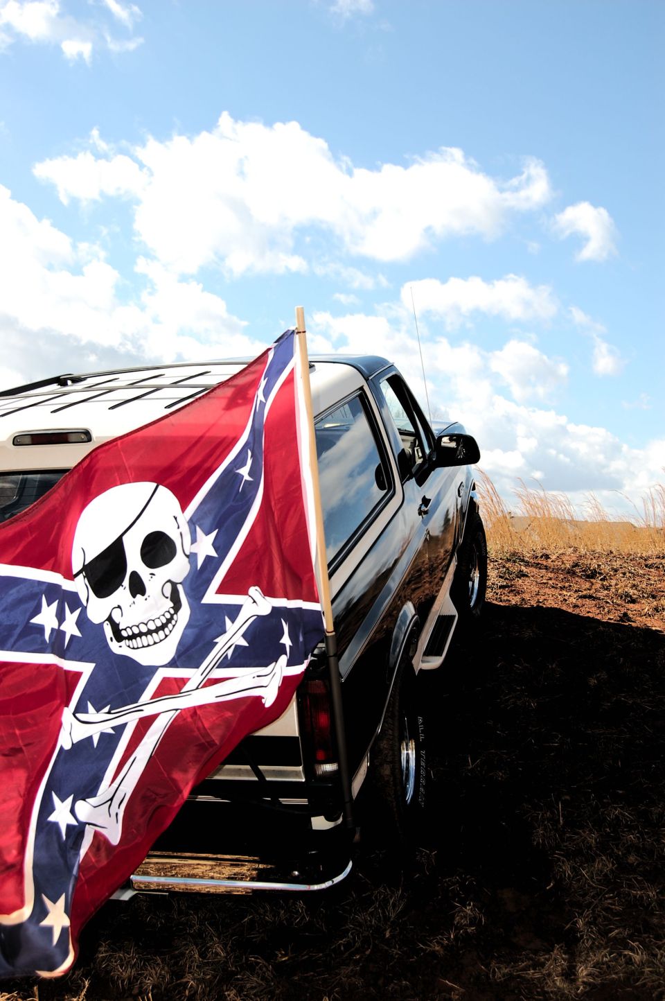 Back of a dark-colored SUV with a Confederate flag flying from the rear. Cloudy sky