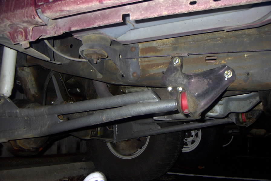 Underbody view of traction bar with red poly bushings under a red vehicle