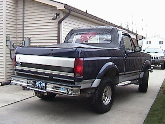 Dark blue Ford Bronco parked in driveway, rear view. Another SUV is parked behind it