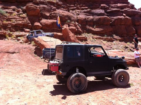 1987 Suzuki Samurai - A black Suzuki Samurai is parked on a dirt trail with other vehicles in the background.