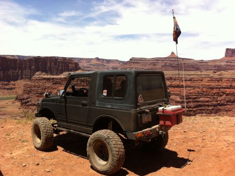 1987 Suzuki Samurai - A 1987 Suzuki Samurai is parked on a dirt road overlooking a vast canyon landscape.