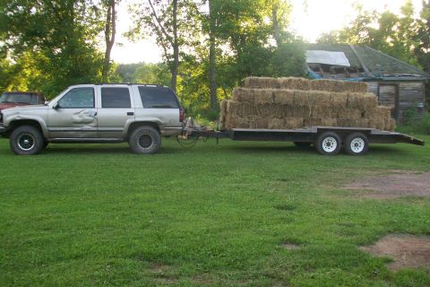 2000 Chevrolet Tahoe - SUV towing a trailer full of hay bales in front of a dilapidated building.