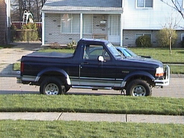 Dark blue 1995 Ford Bronco parked on a residential street, side view. Chrome bumper and silver trim visible