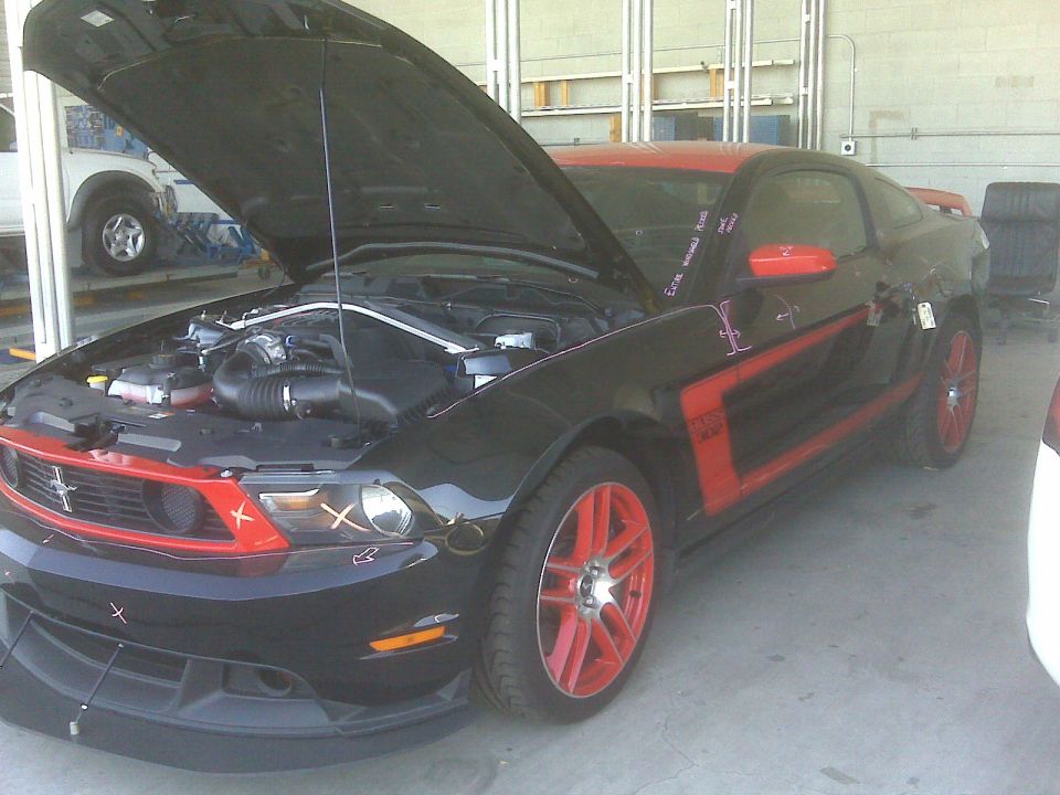 Black Ford Mustang with red accents and hood open, showing engine bay. Red wheels are visible