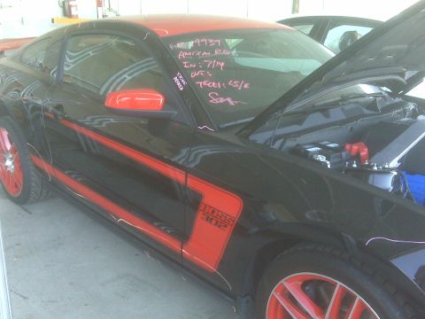 1973 Ford Mustang - A black 2012 Ford Mustang Boss 302 with red accents is parked with its hood open, revealing the engine compartment.