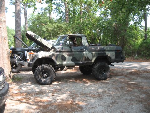 1994 Ford Bronco - A camouflaged Ford Bronco sits parked with its hood open, showing off its lifted suspension and oversized tires.