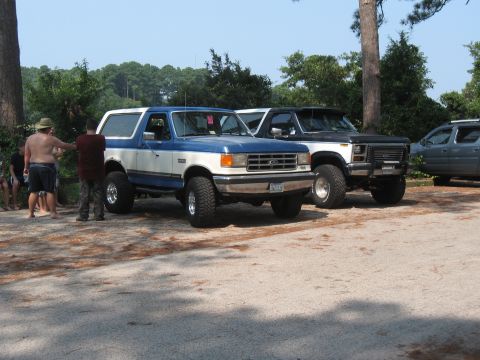 1994 Ford Bronco - Two Ford Broncos, a blue and white 1994 model and a black one, are parked outdoors with people nearby.