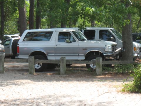 1994 Ford Bronco - This 1994 Ford Bronco is parked on a sandy area, partially obscured by a wooden fence.