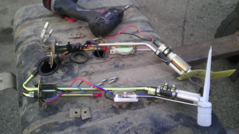 1989 Ford Bronco - A disassembled fuel pump assembly rests on a gas tank, alongside a power drill.