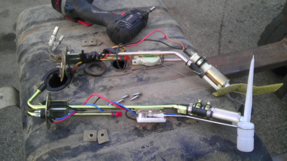 Fuel pump assembly with wiring and hoses on a dirty gas tank, with a drill in the background