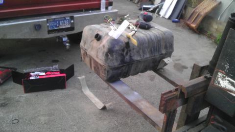 1989 Ford Bronco - A fuel tank is being moved by a forklift, next to a box of new parts and a truck bumper with a license plate.