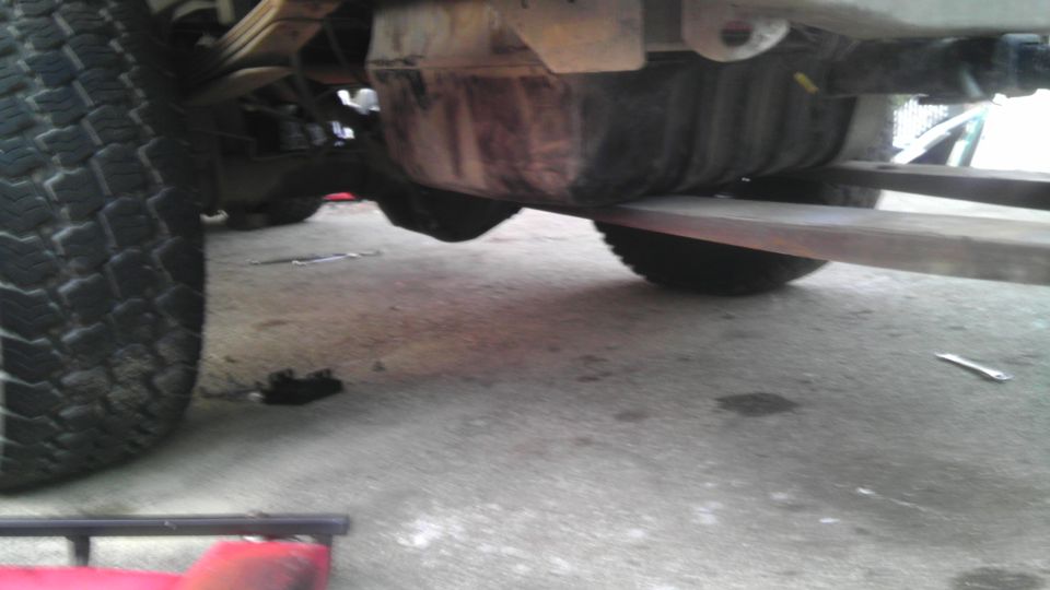 Underside of a vehicle, showing the rear tire, leaf springs, and fuel tank