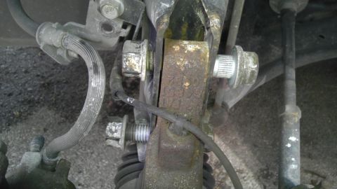 2007 Dodge Caliber - Close-up view of a corroded car suspension part, showing bolts and a brake hose.
