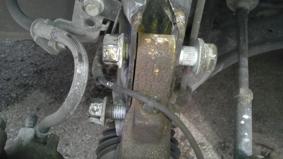 Rusty metal car suspension component with bolts and brake line
