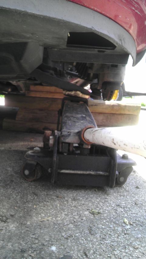 2007 Dodge Caliber - Vehicle being lifted by a jack for repairs, supported by wooden blocks.
