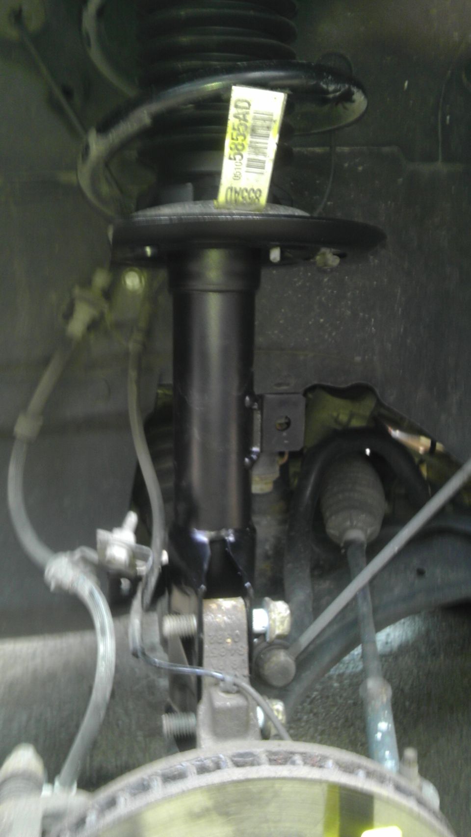Car's front strut assembly with a yellow tag that has numbers on it